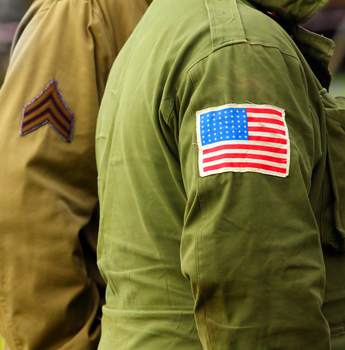 Image of two figures in US Army Jackets, one which has an American Flag patch sewn to the arm