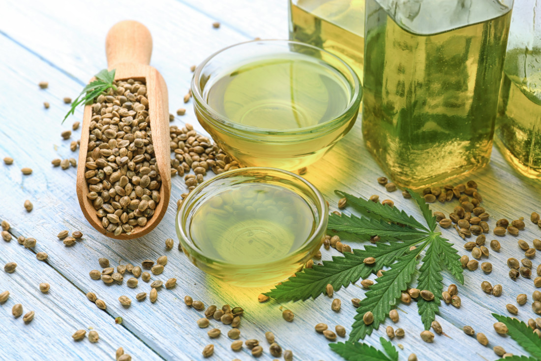 Composition with marijuana leaf, hemp seeds and oil in bowls and bottles on a table