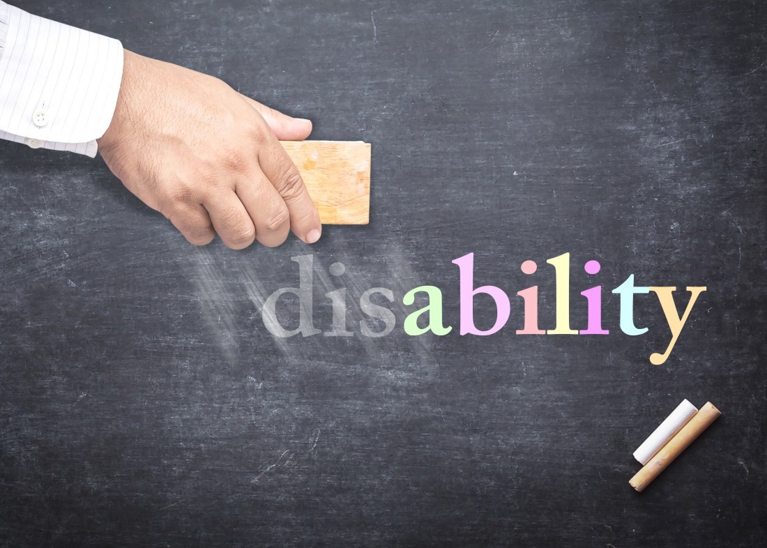 Blackboard with hand holding an eraser starting to erase the word “disability”