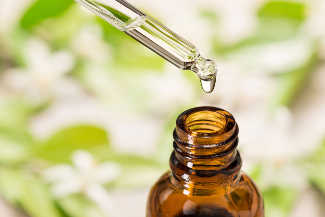 Essential oil falling from glass dropper into a bottle