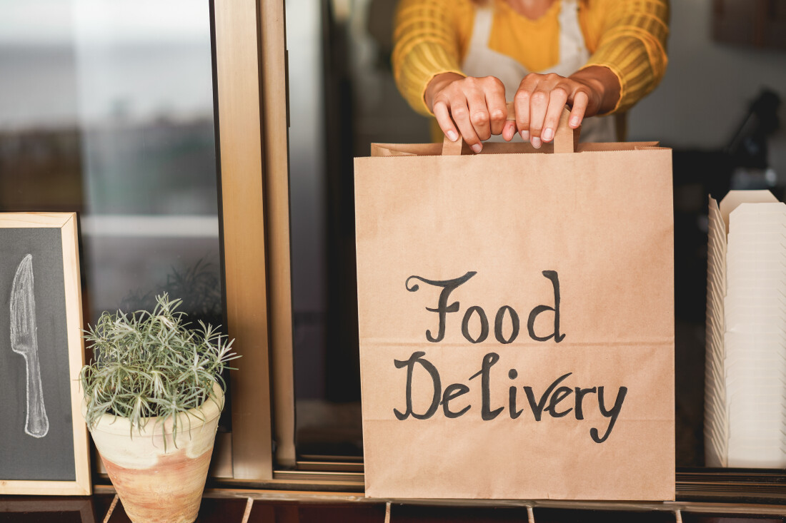 Kitchen worker holding a handled paper bag with “Food Delivery” printed on it