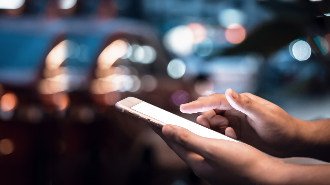 Hands using smartphone at night on city shopping street