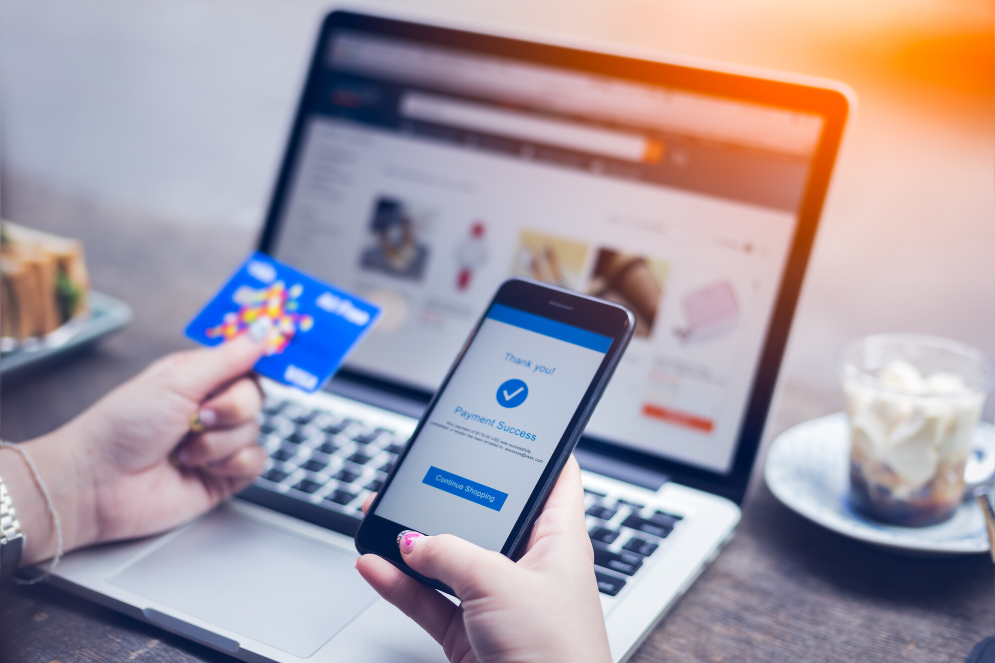 Woman’s hands holding a credit card and smart phone in front of a laptop and a coffee cup