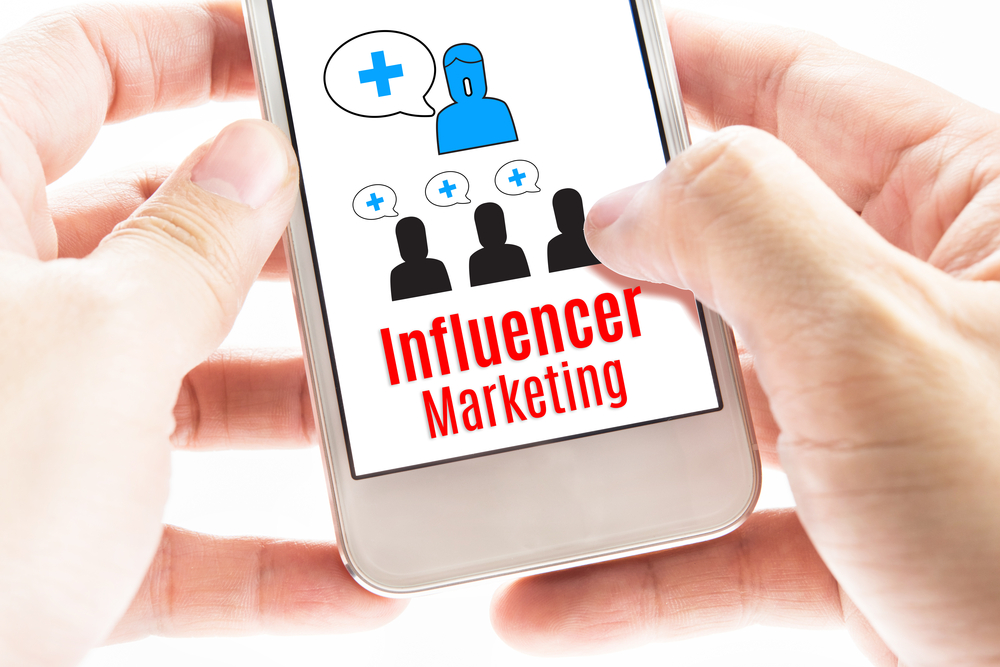 Hands holding a smart phone displaying “Influencer Marketing” and icons of one influencer and three recipients 