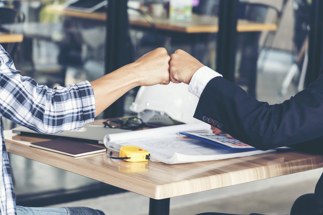 Two people fist bumping over a worktable